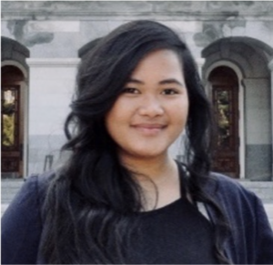 A woman with long black hair wearing a dark sweater and a black shirt standing in front of a neutral background