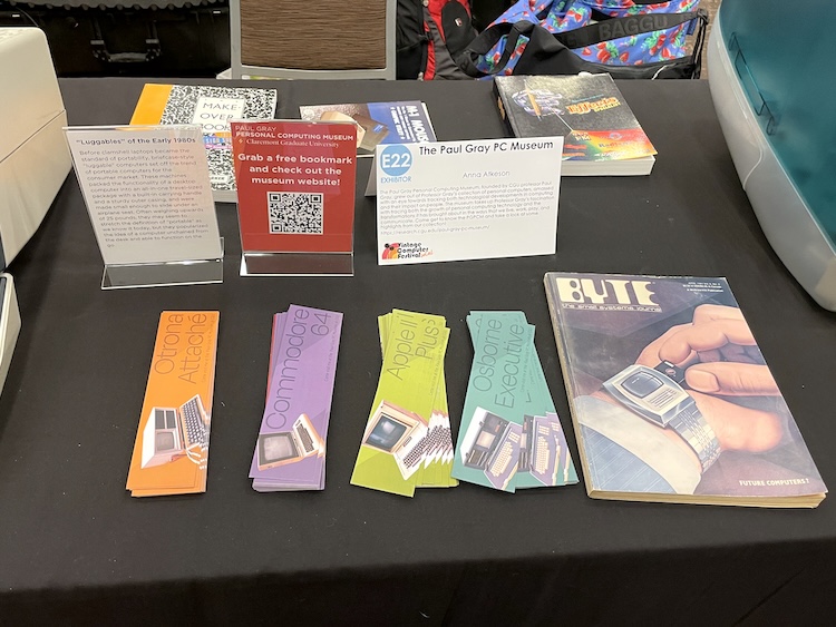 Close up of a section of an exhibition table containing four stacks of promotional bookmarks, a copy of Byte magazine, and a small sign with a QR code to the museum's website.